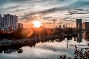 Cityscape with a view on a river, park and a building under construction. Sunset.