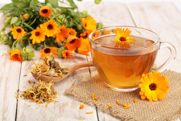Calendula tea with fresh and dried flowers on white wooden background