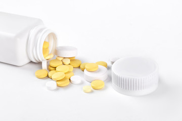 Pills and bottle, white background. Yellow pills and white plastic pills bottle isolated on white background.