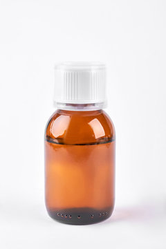 Cough syrup in glass amber bottle. Antipyretic syrup in brown bottle with plastic measuring cup on white background.