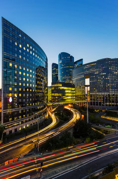 Skyscrapers in Paris business district La Defense. European night cityscape with dynamic street traffic, car lights and glass facades of modern buildings. Economy, finances, transport concept. Toned