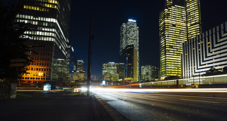 Fototapeta na wymiar Skyscrapers in Paris business district La Defense. European night cityscape with dynamic street traffic, car lights and glass facades of modern buildings. Economy, finances, transport concept. Toned
