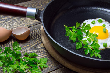 Fried egg with leaves of green onions in a cast iron pan with parsley on wooden background with...