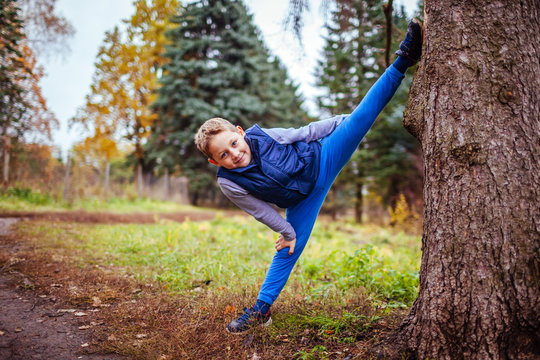 Little boy shows splits standing by the tree in the forest
