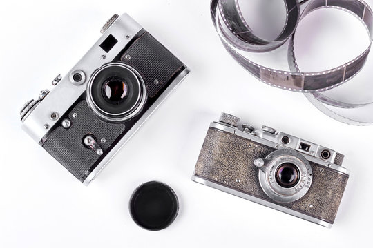 Obsolete cameras on white background. Old-fashioned cameras, film tape, cap. Two vintage film cameras on white background.