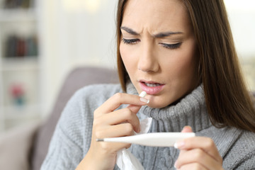 Woman with fever looking thermometer eating a pill