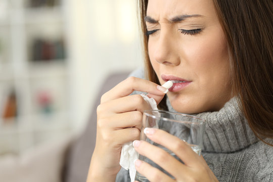 Woman suffering flu symptoms eating a pill