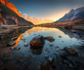 Wonderful landscape with high rocks with illuminated peaks, stones in mountain lake, reflection,...