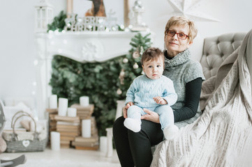 Grandmother and child sitting in a chair by the fireplace near Christmas tree