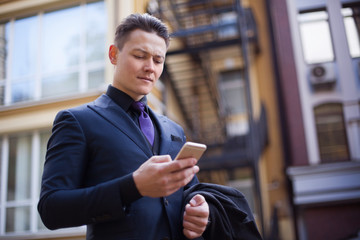 A frustrated businessman in a suit reads a message on the phone in the street.