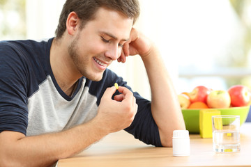 Happy man taking a vitamin pill at home