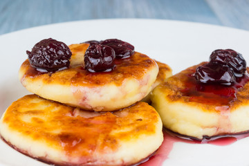 Delicious cheese pancakes with cherry jam on a rustic wooden background