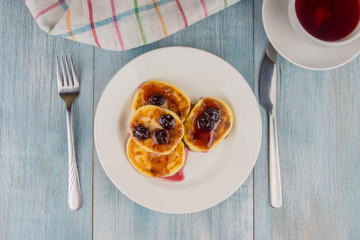 Delicious cheese pancakes with cherry jam on a rustic wooden background with fruit tea