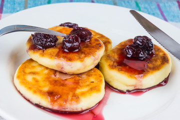 Delicious cheese pancakes with cherry jam on a rustic wooden background