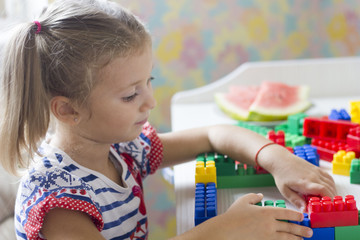 little girl in dress sits at table and collect the colored blocks