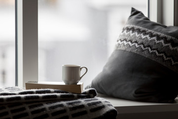 Cozy coffee cup, pillow, and blanket in a window seat