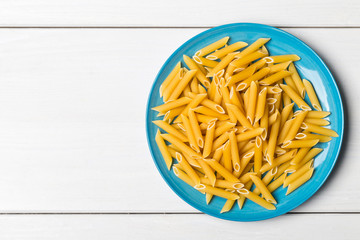 Heap of dried, raw, uncooked penne pasta on plate on table