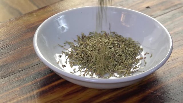Dried thyme falling into a spice dish