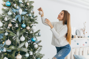 A beautiful girl is decorating a christmas tree.