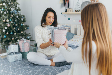 Two happy, stylish and beautiful girl friends presented each other with Christmas gifts and opened them up in the vintage white room.