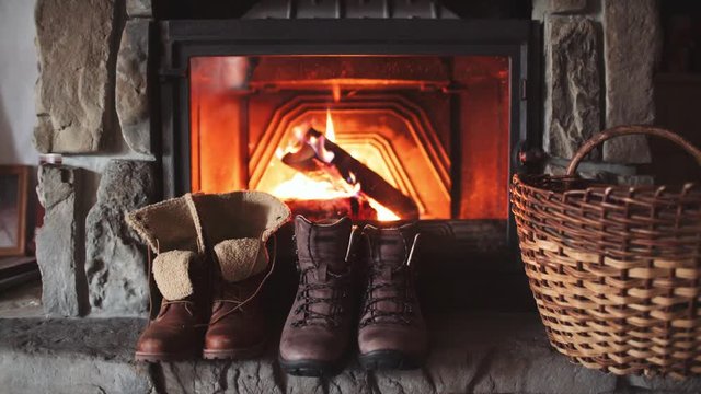 Couple Winter Boots Drying in front of a Burning Warm Fireplace - 4K. Family vintage folk boots getting warm near the fireside in a cabin. Warm cozy fireplace in the authentic chalet. 