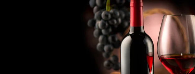 Gordijnen Wijn. Fles en glas rode wijn met rijpe druiven op zwarte achtergrond © Subbotina Anna