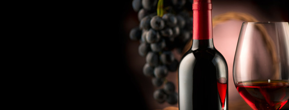 Wine. Bottle and glass of red wine with ripe grapes over black background