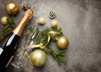 A bottle of champagne with various chocolate candies of a round shape an empty glass and spruce...