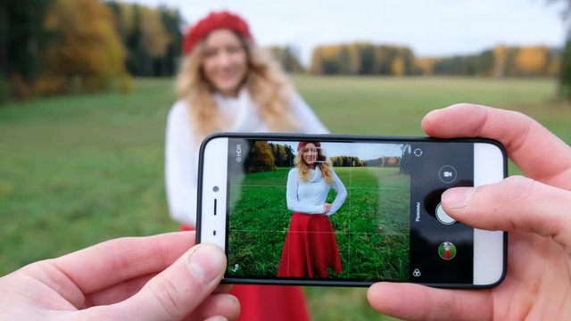 Young man photographs the new modern smartphone beautiful Caucasian girl on the nature. Girl posing in different poses and smiles to the happy moments in life.