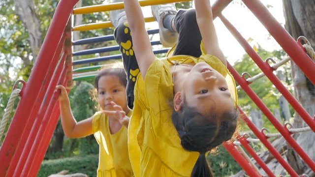 Cute asian little child girl having fun to hang on the steel bar to exercise at playground with flare in summer time in slow motion
