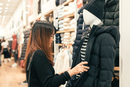 Half body shot of a happy asian young woman with shoulder bag looking at clothes hanging on the rail inside the clothing shop. Shopping, fashion, style and people woman concept.