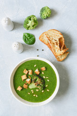 Broccoli cream soup with croutons and pine nuts in white bowl. Table top view, vertical