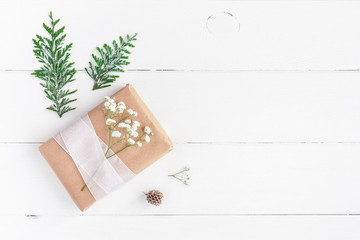 Christmas border. Christmas gift, pine cone, gypsophila flowers, thuja branches on white wooden background. Flat lay, top view, copy space
