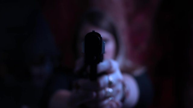 Color graded female assassin aiming pistol at camera in dark cinematic room
