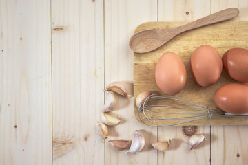 egg on wooden background and garlic, whisk, top view