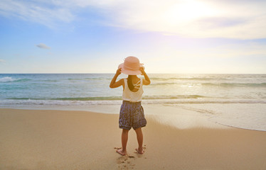 Naklejka na ściany i meble Rear view Adorable little girl wear straw hat relax at the beach at sunset.