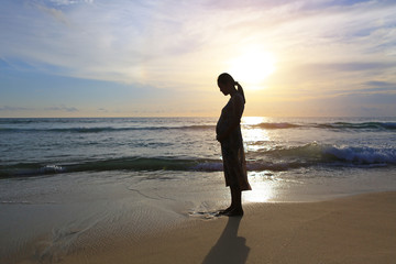 Silhouette of pregnant woman standing on the beach at sunset.