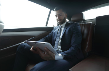 businessman working in the back seat of a car and using a tablet