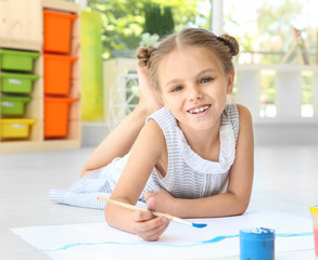 Little girl lying on floor in light room and painting