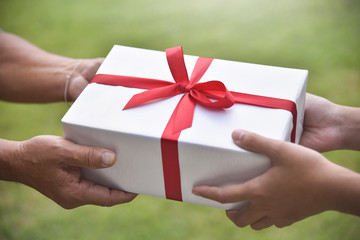 Asian woman giving a white gift box to elderly man.