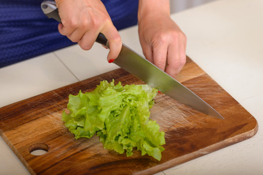 Woman cuts salad on wooden board