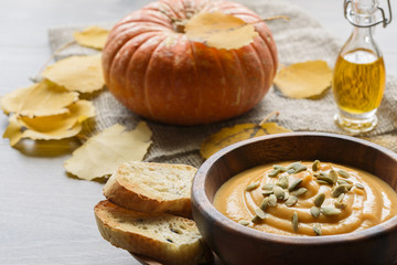 Pumpkin soup in a wooden bowl, with autumn leaves and pumpkin