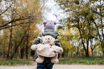 Little girl in autumn forest with teddy bear backpack.