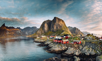 Norwegian fishing village at the Lofoten Islands in Norway. Dramatic sunset clouds moving over steep mountain peaks - obrazy, fototapety, plakaty
