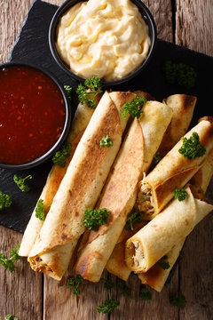taquitos with chicken and cheese close-up, as well as sauces. Vertical top view
