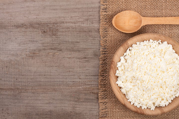 Cottage cheese in a wooden bowl with sour cream on old wooden background with copy space for your text. Top view