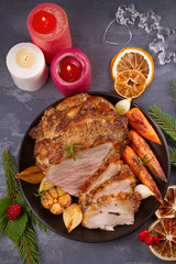 Roasted sliced Christmas ham with vegetables and festive decoration on grey rustic background, view from above, top, vertical