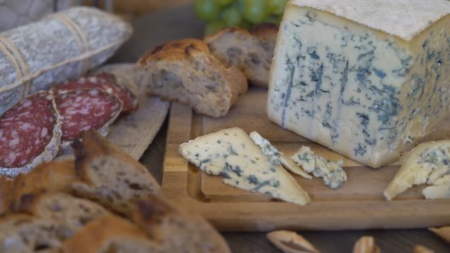 appetizing sausage loaf in a bag of marble fabric. the sausage rests on a wooden table of brown color. In the background a baguette, cheese with green mold and a large bunch of white grapes with a