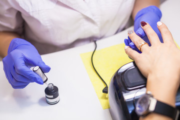 Close-up of a manicure master in sterile blue gloves paints a girl's nails with a protective nail polish on a white clean table