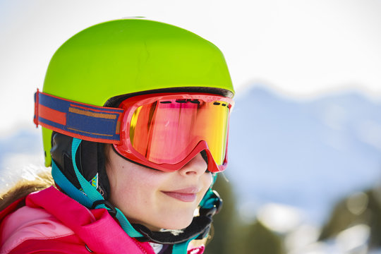 Portrait of happy young girl sitting in the snow with ski in winter time, ski slope in the background.